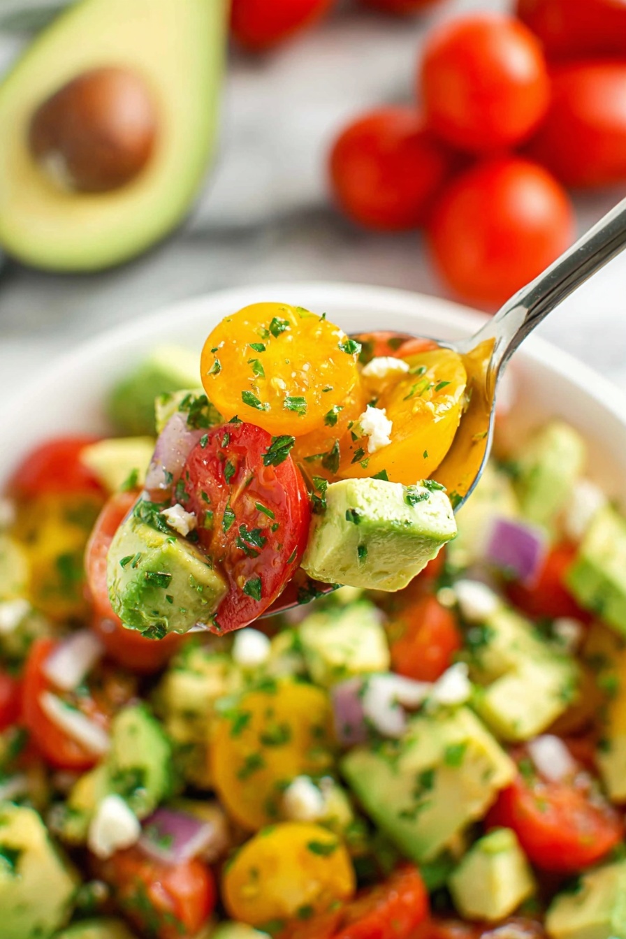 A close-up top view of a white bowl filled with a colorful salad. The salad has two main layers: a base layer of chopped green cucumbers with a fresh, slightly wet texture, mixed with diced light green avocado pieces, and on top, a layer of halved small red cherry tomatoes and golden yellow tomatoes, all mixed evenly. Small white crumbles of cheese are scattered over the top, adding a crumbly texture. The salad is sprinkled with finely chopped green herbs, giving a fresh look. Around the bowl, there is half an avocado with the seed still inside and a few small red cherry tomatoes on a white marbled surface. Photo taken with an iphone --ar 2:3 --v 7