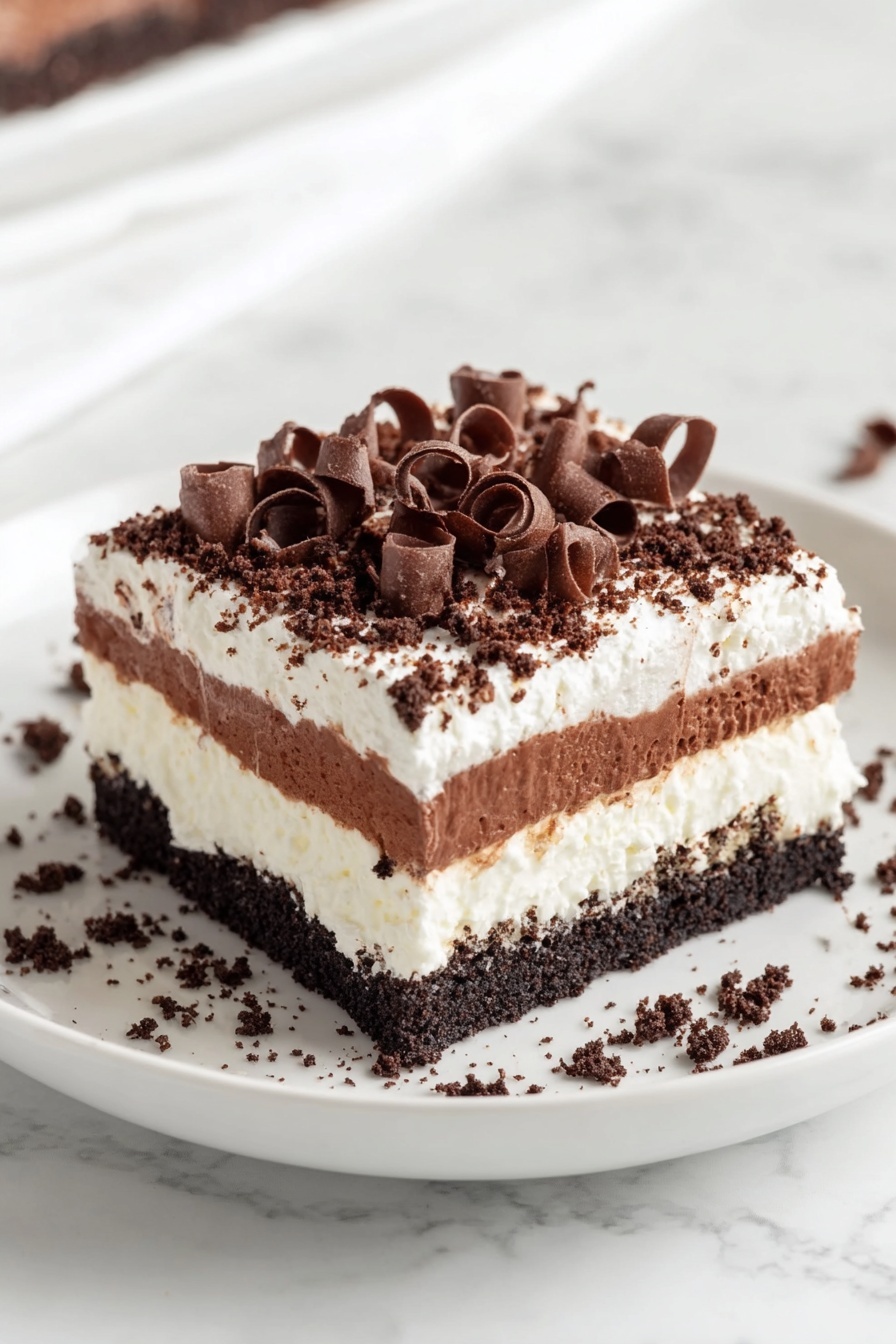 A square piece of layered dessert sits on a white plate with a white marbled background. The bottom layer is dark and crumbly, followed by a thick white creamy layer. Above this is a rich, smooth chocolate layer, topped again with a thin white cream layer. The top is covered with a dark crumbly texture, sprinkled generously with small chocolate curls that add a decorative touch. Some chocolate curls also scatter around the base on the plate. photo taken with an iphone --ar 2:3 --v 7