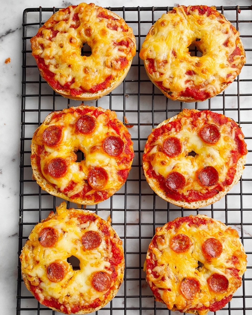 Six mini bagel pizzas are placed on a black wire rack over a white marbled surface. Each bagel is topped with a layer of bright red tomato sauce spread evenly over the top half of the bagel, followed by a thick, bubbly layer of melted golden-yellow cheese that has browned slightly from baking. Three of the bagel pizzas have small round slices of brown sausage scattered on top of the cheese. The bagels have a light, slightly toasted brown crust visible around the edges. The wire rack grid creates a neat pattern beneath the bagels, and the photo has a clean, bright look. photo taken with an iphone --ar 2:3 --v 7
