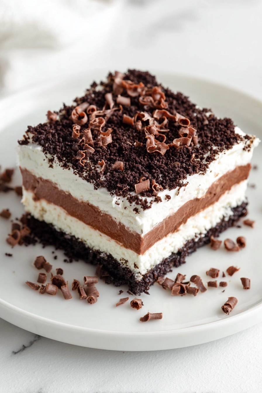 A square dessert with four layers sits on a white plate over a white marbled surface. The bottom layer is dark and crumbly, made of crushed cookies. Above it is a thick white cream layer, smooth and dense. Next, a rich chocolate layer adds a darker brown, silky texture. On top, there is another white cream layer, light and fluffy. The dessert is covered with tiny dark cookie crumbs and decorated with tight chocolate curls scattered on top and around the plate. Photo taken with an iphone --ar 2:3 --v 7