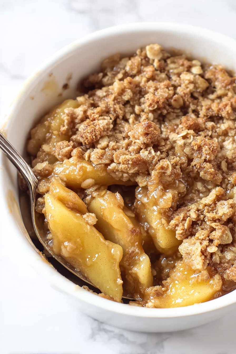 The image shows a white bowl filled with a warm apple crumble dessert. The dish has two main layers: the bottom layer is made up of soft, sliced apple pieces that are golden and slightly glossy with syrup, while the top layer is a crumbly, brown oat topping with a rough, grainy texture. The oat topping is slightly uneven, with small chunks and a mixture of light and darker brown shades, giving it a baked look. A spoon is partially submerged in the apple layer, breaking through the oat topping, showing the juicy filling underneath. The background is a white marbled surface. Photo taken with an iphone --ar 2:3 --v 7