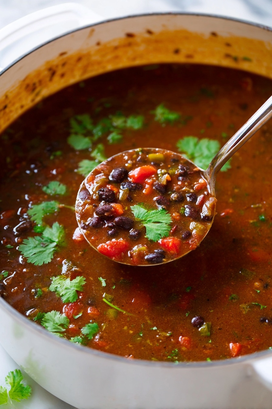 A white pot filled with rich brown black bean soup showing visible whole black beans and small pieces of red bell pepper mixed in, garnished with fresh green cilantro leaves scattered on top. A silver ladle is resting inside the pot on the left side. The pot sits on a wooden board over a light blue cloth, with bright green lime wedges placed near the bottom right corner. In the background on a white marbled surface, there are light brown tortilla chips on the upper left and a bunch of fresh cilantro leaves on the upper right. Photo taken with an iphone --ar 2:3 --v 7