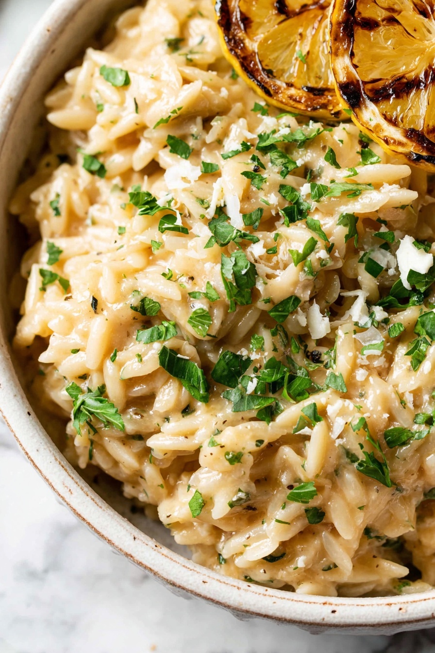 A close-up image of creamy orzo pasta layered in a white bowl with a slightly rough edge; the orzo is light beige with small visible herbs mixed throughout, giving it a speckled green and black look. On top, there is a sprinkle of finely chopped fresh green herbs and small bits of white cheese, adding color contrast. To the side, a slice of grilled lemon with a golden-brown charred texture is resting over the orzo. The background shows a white marbled surface, adding a soft, clean look. photo taken with an iphone --ar 2:3 --v 7