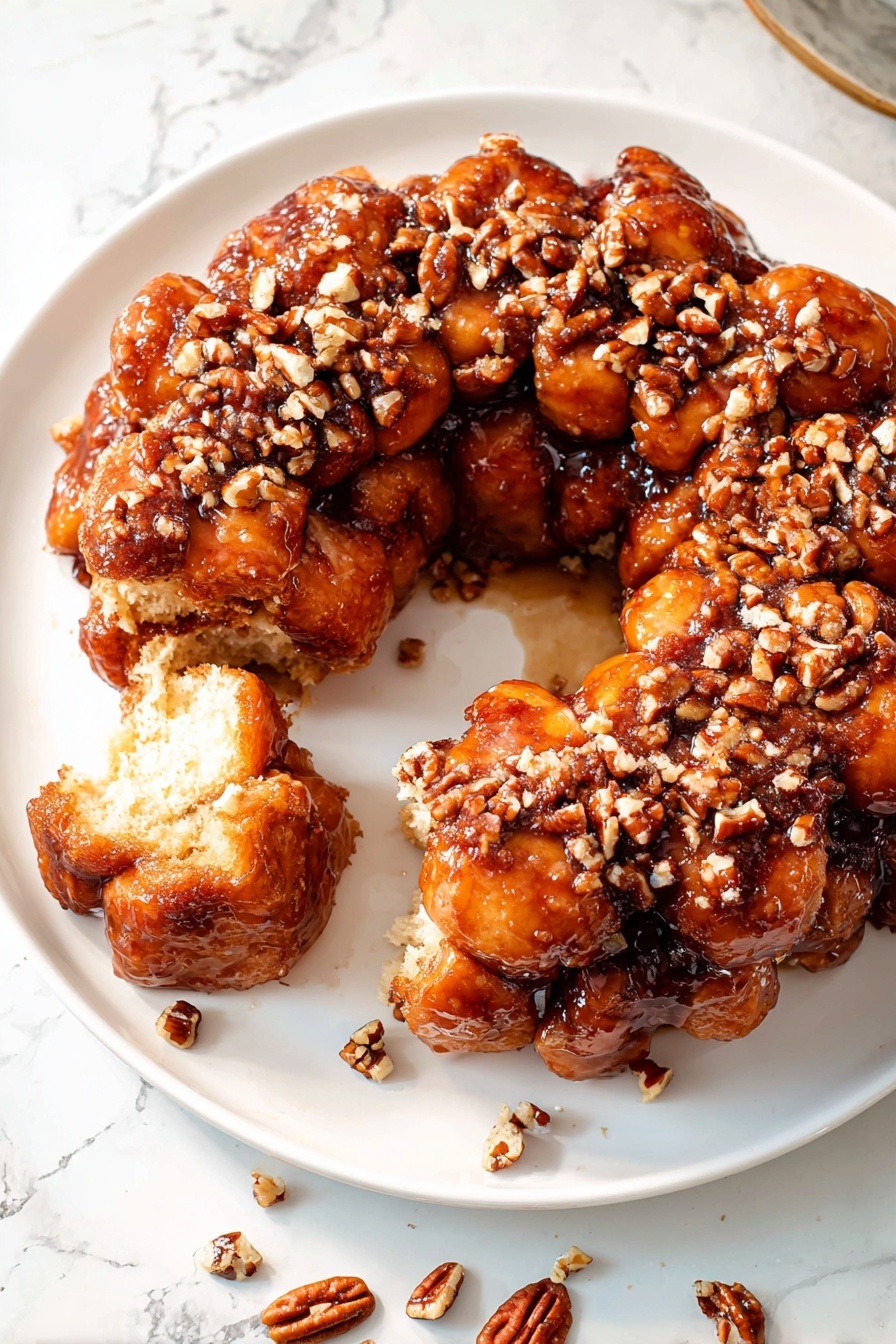A white plate holds a ring of sticky monkey bread made of many small, soft dough balls stuck together, coated in shiny brown cinnamon glaze. The top of the bread is covered with scattered chopped pecans, adding a crunchy texture. One dough ball is pulled away, showing the soft, light inside and the gooey glaze holding the pieces together. Extra chopped pecans are scattered around the plate. The plate sits on a white marbled surface. photo taken with an iphone --ar 2:3 --v 7