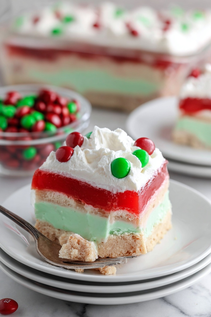 This image shows a square dessert with five layers on a white plate. The bottom layer is a beige, crumbly crust with small nut pieces. Above it is a thick, smooth mint green layer. Next is a white fluffy layer with some small air holes, followed by a semi-translucent bright red jelly layer. The top layer is a thick white whipped cream with a swirled texture, decorated with red and green round candy pieces scattered on top. The background is a white marbled texture. Photo taken with an iphone --ar 2:3 --v 7