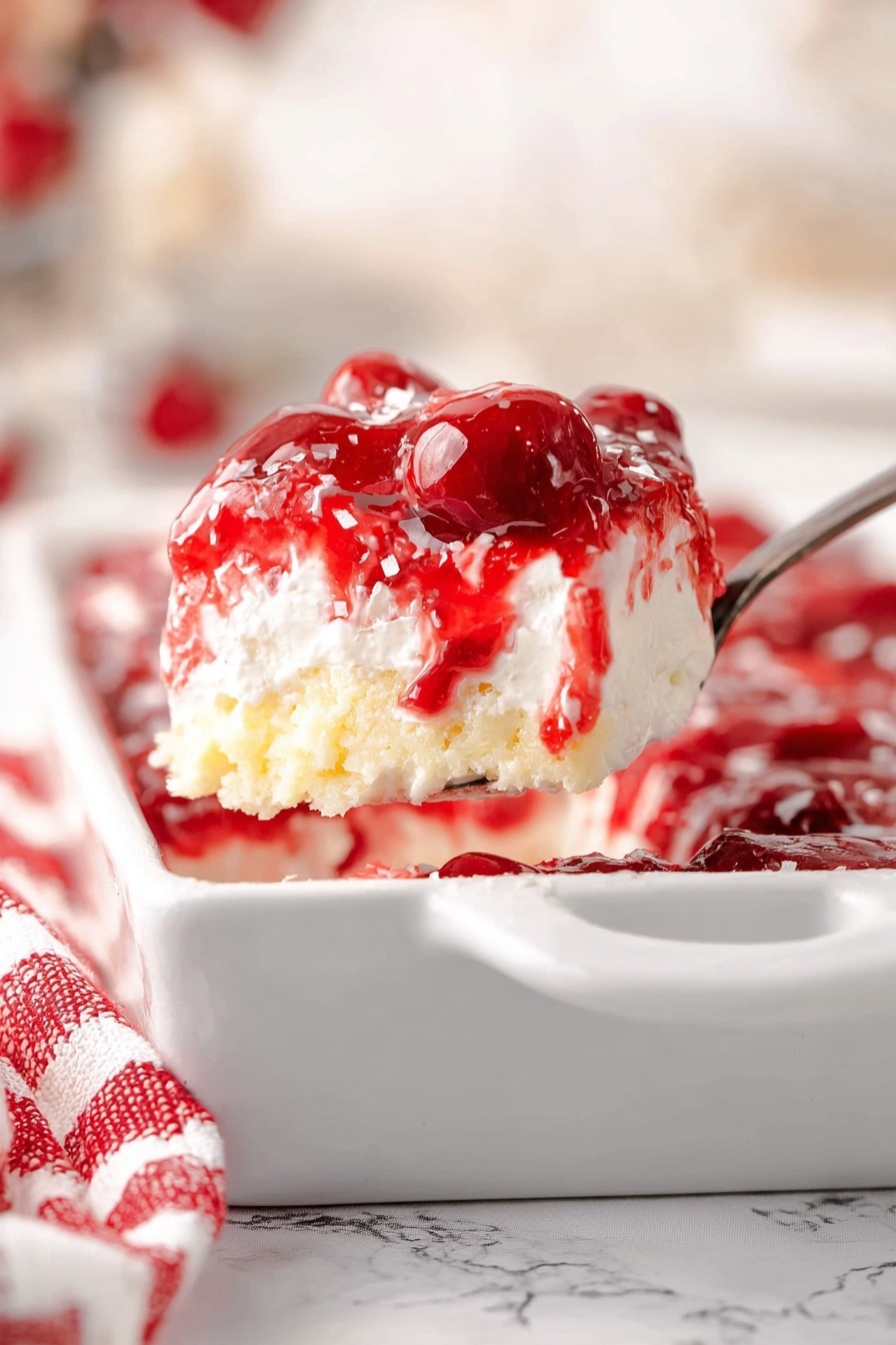 The image shows a close-up of a spoon holding a scoop of layered dessert. The dessert has three layers: the top layer is bright red cherry topping with visible whole cherries and shiny syrup; the middle layer is white and creamy, smooth in texture; the bottom layer is light yellow, resembling soft cake or biscuit pieces. The dessert is inside a white rectangular dish with a handle, and there is a red and white striped cloth nearby. The background has a soft focus with light colors and a white marbled texture surface. photo taken with an iphone --ar 2:3 --v 7