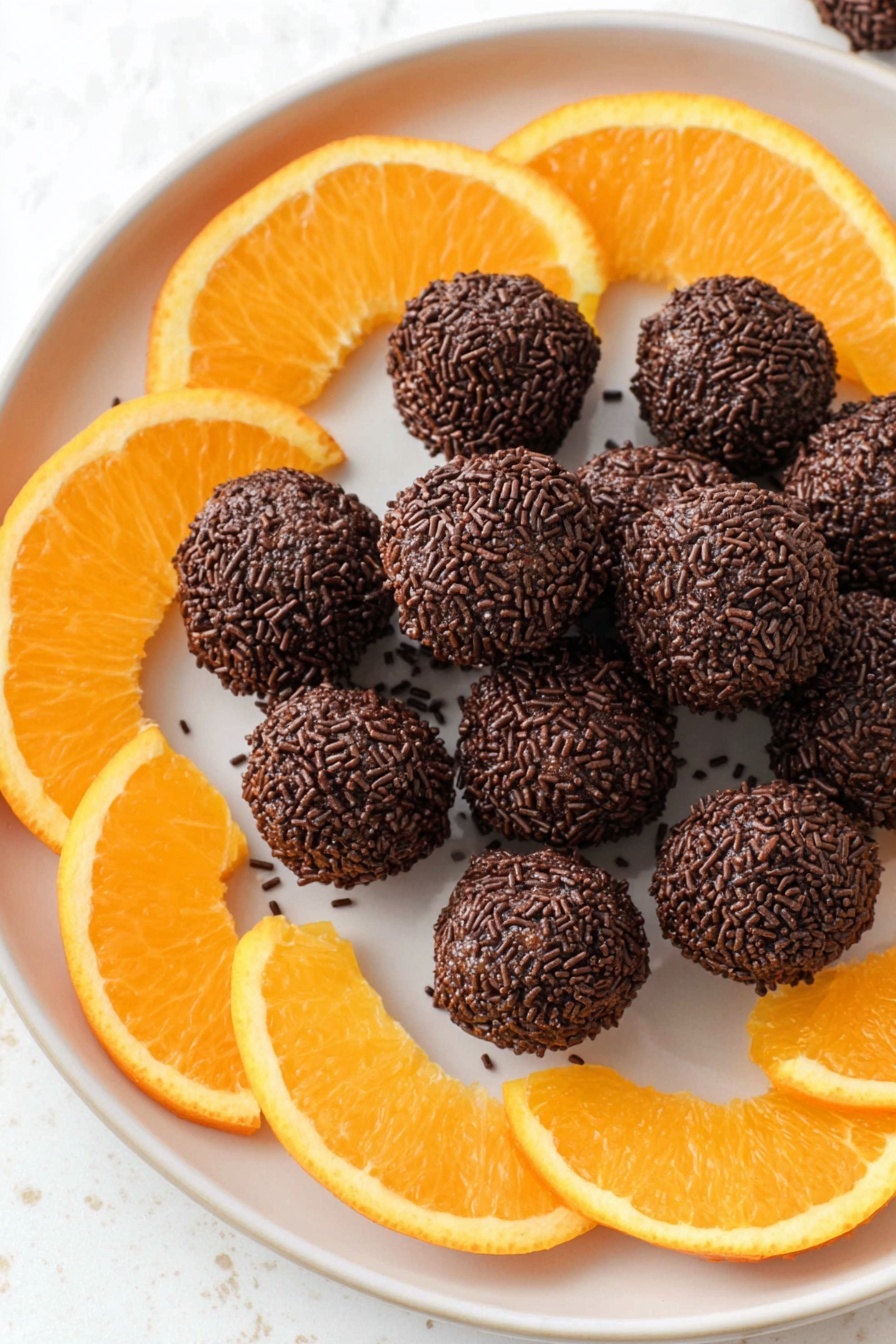 A clear white plate holds a pile of small round chocolate balls covered in dark chocolate sprinkles, creating a rough texture. Around the pile, bright orange slices with juicy, slightly translucent flesh and a soft rind alternate, framing the chocolate balls evenly. The plate sits on a white marbled surface that adds a soft, clean look to the composition. The image is bright and focused, showing the contrast between the dark chocolate texture and the vibrant orange slices. photo taken with an iphone --ar 2:3 --v 7
