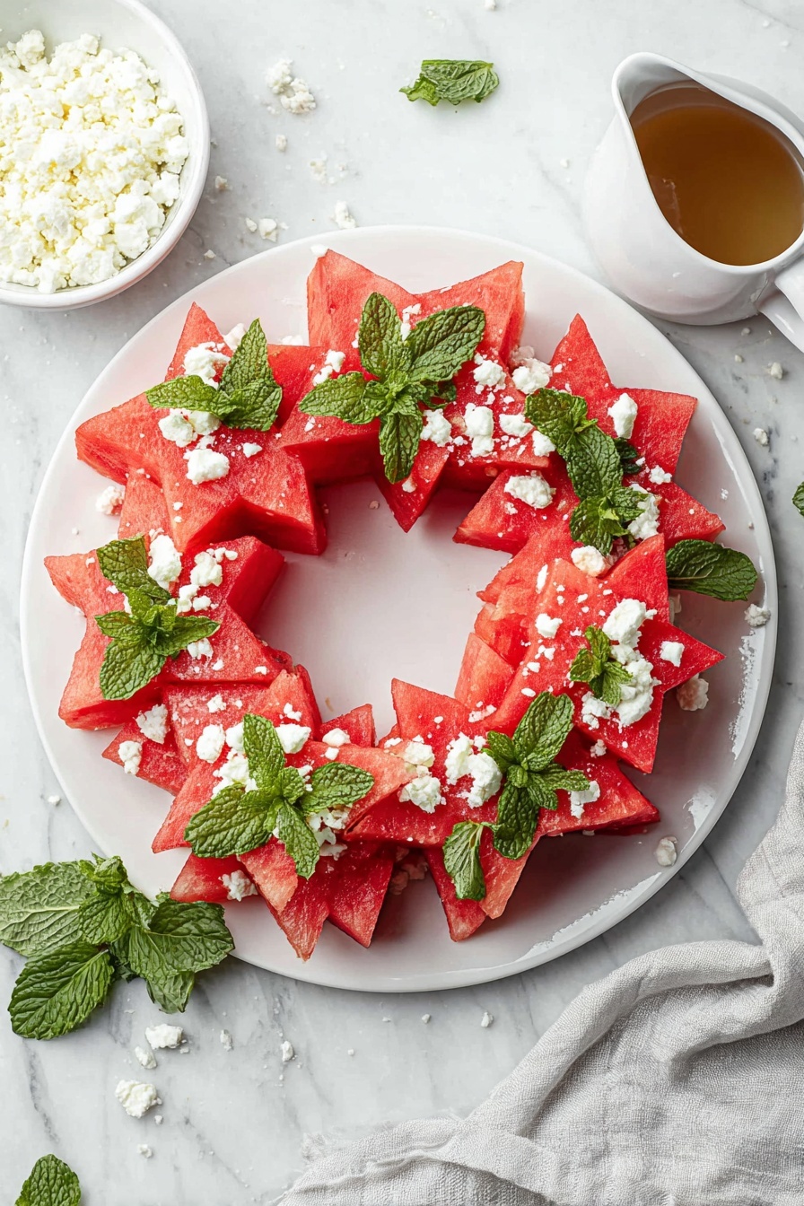 A white round plate holds a festive wreath made of watermelon slices shaped like stars and triangles arranged in a circle. Bright green mint leaves are placed between the watermelon pieces, adding contrast. White crumbled cheese is sprinkled all over the watermelon and mint, giving texture and color. The plate sits on a white marbled surface with a small white bowl of crumbled cheese on the side and a white container holding a light brown liquid above. A soft gray cloth is draped beside the plate. Photo taken with an iphone --ar 2:3 --v 7