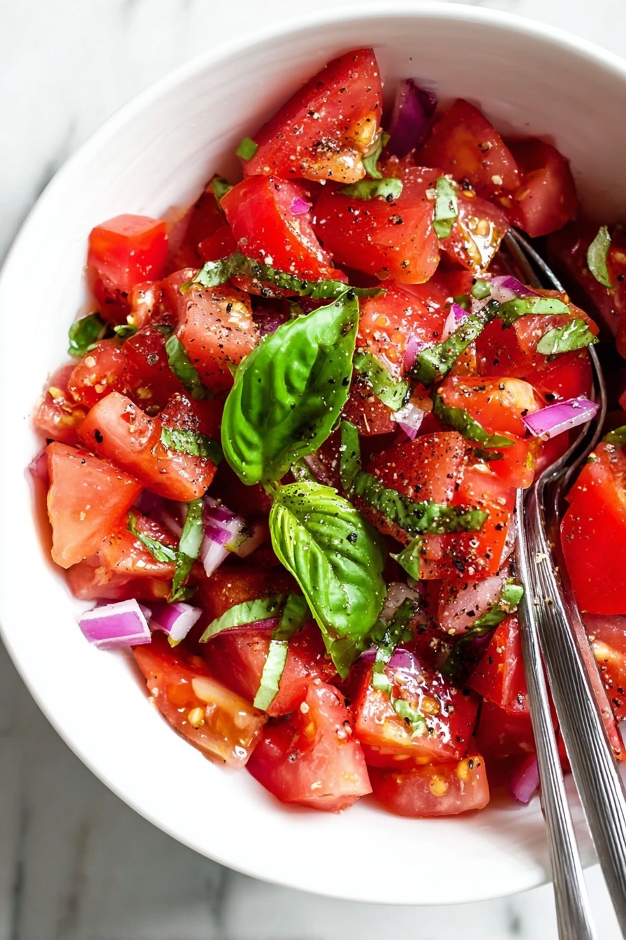 A white bowl filled with a fresh tomato salad showing bright red tomato chunks as the main layer, mixed with small pieces of purple onion scattered throughout. On top are large, bright green basil leaves adding a fresh look. The salad is sprinkled with black pepper and a light dressing that gives a slight shine to the ingredients. Two metal forks rest on the edge of the bowl. The bowl is set on a white marbled surface. Photo taken with an iphone --ar 2:3 --v 7