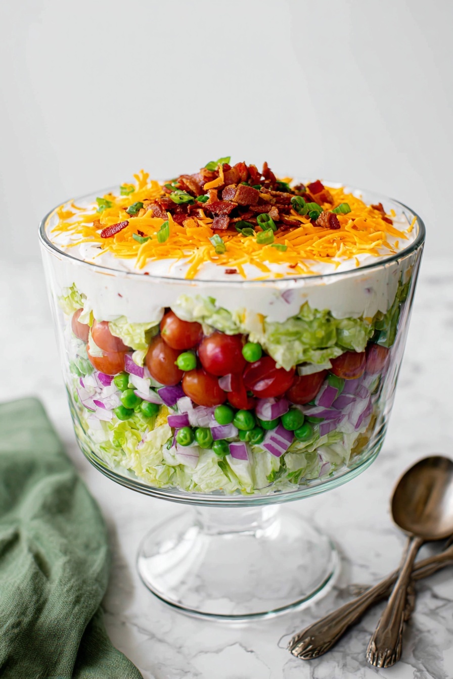 A clear glass bowl on a glass pedestal shows a salad with six layers. The bottom layer is light green lettuce pieces, above that is a layer of chopped purple onions. Next, there are halved red cherry tomatoes mixed with green peas. A thick white creamy layer comes after, topped by a shredded orange cheese layer. The topmost layer has small bits of crispy bacon, giving a crunchy texture. The bowl sits on a white marbled surface with two spoons and a green cloth nearby. photo taken with an iphone --ar 2:3 --v 7