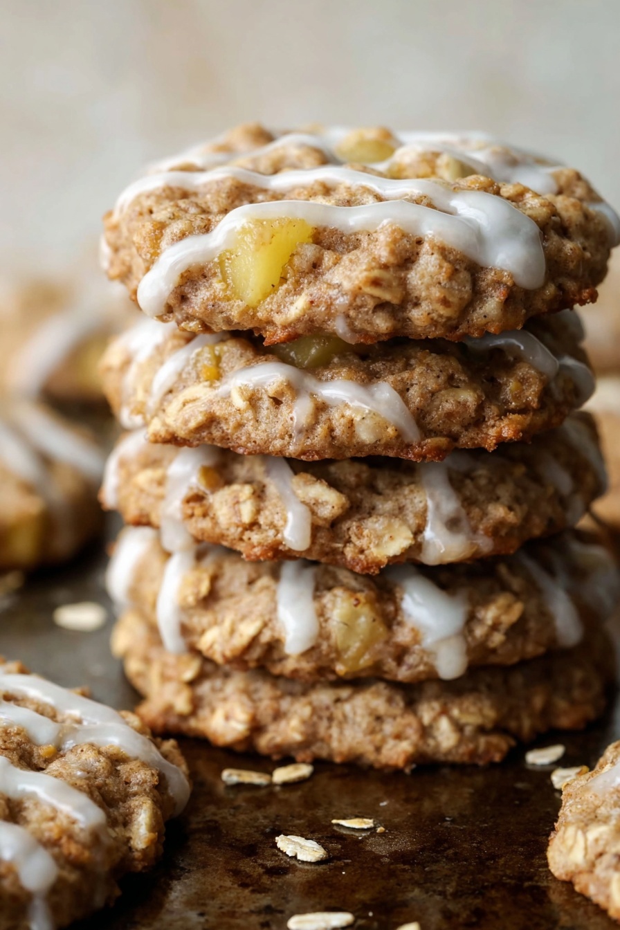 A single oatmeal cookie with visible chunks of light yellow apple embedded in it sits on a rustic, speckled baking tray. The cookie is round and textured with a rough, bumpy surface showing the oats and apple pieces. White icing is drizzled loosely in thin stripes across the top, contrasting with the cookie’s golden-brown and light tan shades. The background is a white marbled texture. photo taken with an iphone --ar 2:3 --v 7
