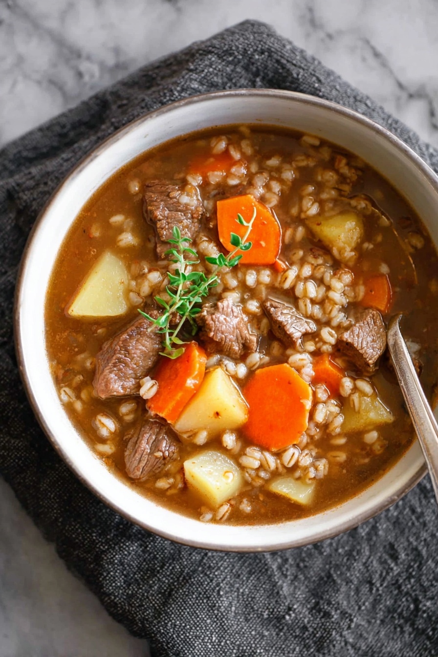 A white bowl filled with a brown broth soup containing chunks of tender meat, bright orange carrot slices, and pale yellow potato pieces, all mixed with small grains of barley. On top of the soup rests a small green herb sprig, adding a fresh touch. A silver spoon is partially submerged on the right side of the bowl, which sits on a gray textured cloth. The background is a white marbled surface. photo taken with an iphone --ar 2:3 --v 7