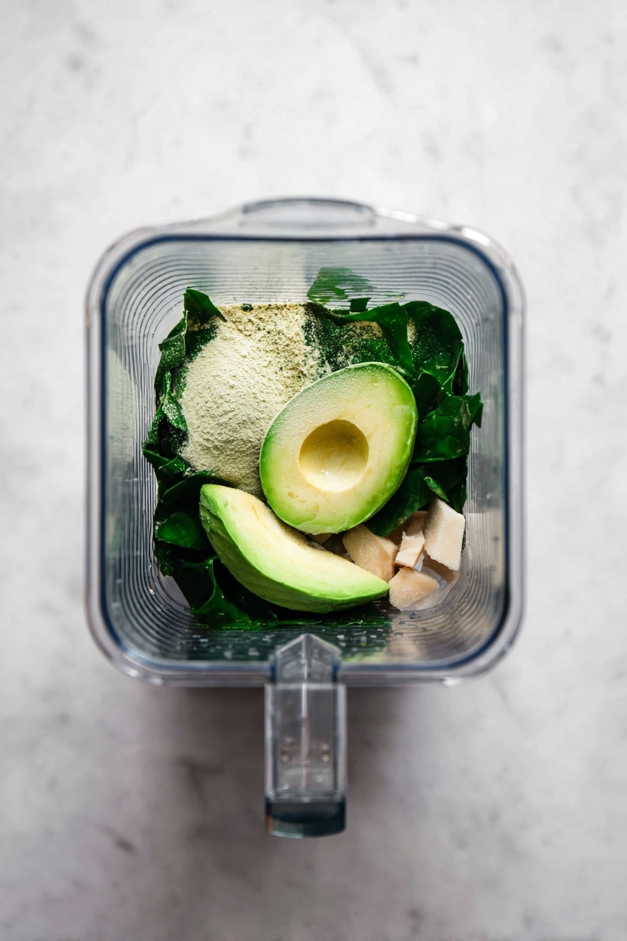A clear glass is filled with a thick, light green smoothie being poured from a clear container above. The smoothie has a smooth, creamy texture. Around the glass, there are fresh dark green spinach leaves on a light brown wooden board. In the background, a yellow banana and a halved avocado with its brown seed are visible, all set against a white marbled surface and white tiled wall. Photo taken with an iphone --ar 2:3 --v 7